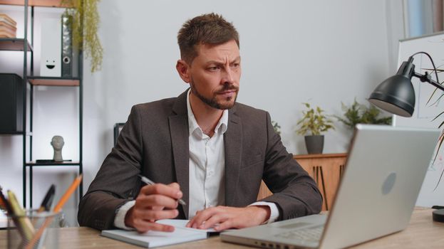Businessman lawyer in suit working on laptop computer online, writing notes in planner notebook at office workplace desk. Professional freelancer student man. Remote education, study, learning lessons