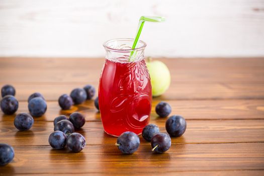 Sweet natural plum drink in a glass with a straw on a wooden table