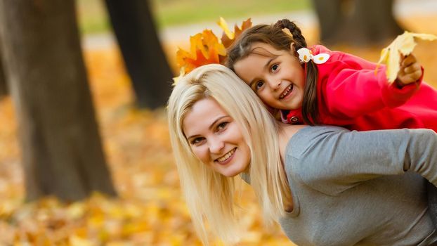 Happy family: mother and child little daughter play cuddling on autumn walk in nature outdoors