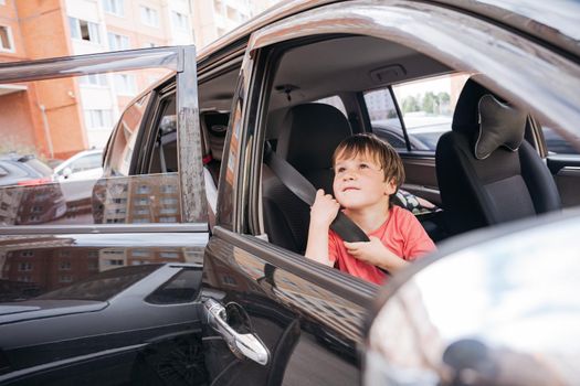 Pre-school boy wearing pink t-shirt sitting in he car and looking with curiosity while holding the safety belt. High quality photo