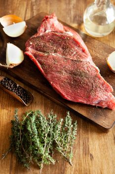 Top view of a chunk of red meat on vintage cutting board next to a bottle of virgin olive oil. Juicy meat.