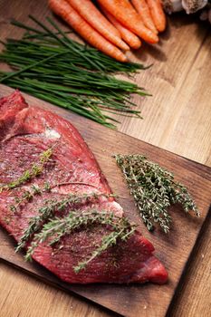 Rosemary on delicious stake next to fresh vegetables on rustic wooden table. Cooking dinner. Black pepper.