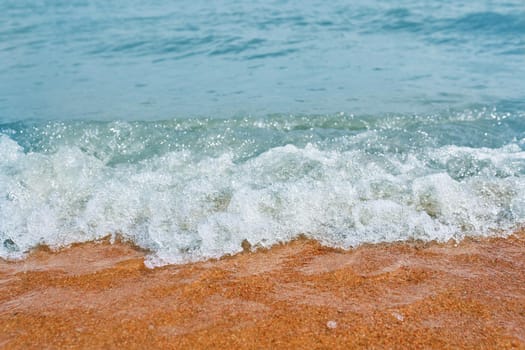 Sandy beach with waves from the sea. Ocean water close up.