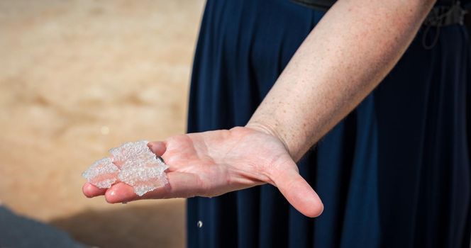 Flower of salt, is a salt that forms as a thin, delicate crust on the surface of seawater in the hand of a women, freshly collected from the salt field. Flower of sea salt crystals isolated on hand.