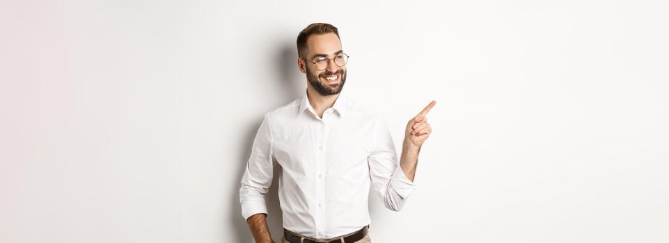 Confident businessman looking satisfied and pointing finger left, showing company banner, standing over white background.