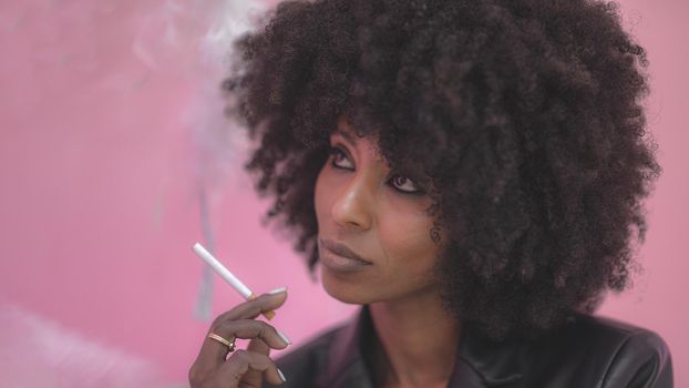 Young attractive African woman with happy cheerful smile smoking in studio