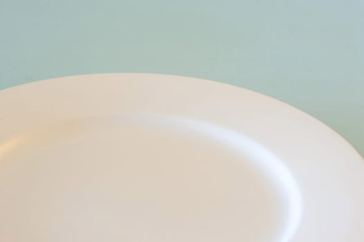 Partial view of an empty clean white dinner plate over a blue background for food placement