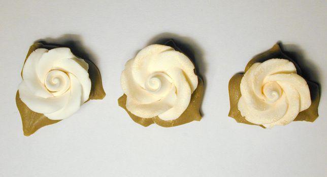 Three icing sugar roses for decorating cakes and confectionery viewed from overhead in a row on a grey background