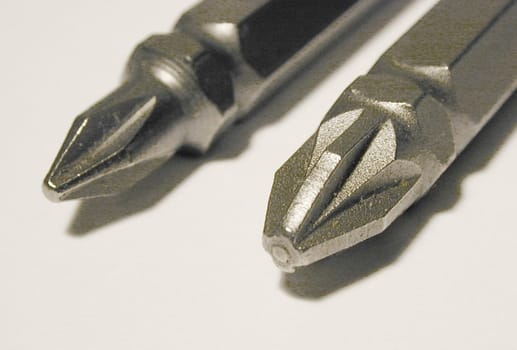 Two new screw bits of Philips and Pozidriv types, viewed in macro close-up on white surface