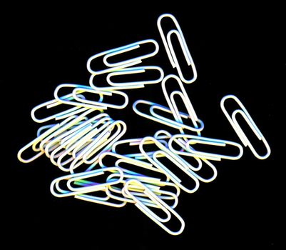 Scattered pile of white paperclips for filing documents and making attachments lying on a black background, overhead, view