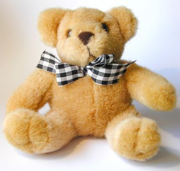 Soft cuddly plush toy teddy bear wearing a black and white checkered bow tie sitting against a white background
