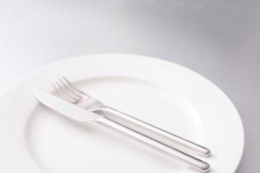 Empty clean generic white plate and silver cutlery with a knife and fork neatly arranged in the centre in a cropped view