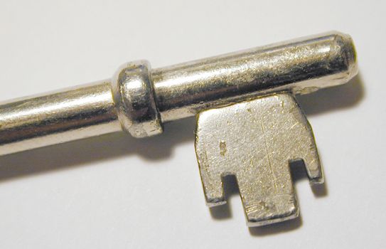 Metallic lever lock key with collar and symmetrical wards, close-up with shadow and copy space on gray