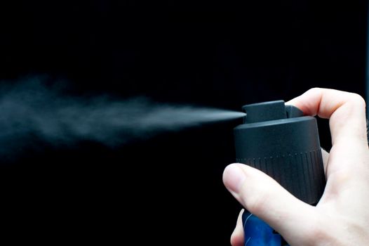 spraying a can of deodorant on a black background