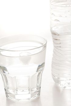 Glass of clean fresh bottled water with the unlabeled plastic water bottle standing alongside on white
