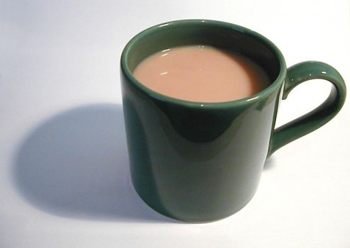 Close-up of a green porcelain mug full of hot coffee with milk, with shadow, on grey