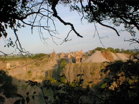 View of an open cast quarry through trees in an concept of exploiting natural resources, mining and industry