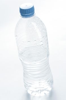 Plastic bottle of cold fresh pure mineral water with beaded condensation on the surface and a blue cap, unlabeled on white