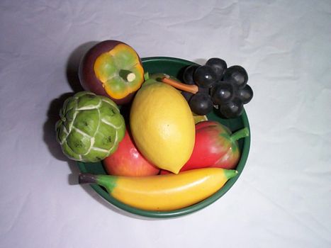 Bowl of fake fresh fruit with colorful wooden imitations viewed from overhead over a grey background