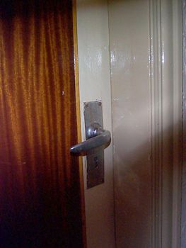 Detail of Silver Colored Door Handle on Closed Door with Large Curtained Window, Partially Obscured by Shadow