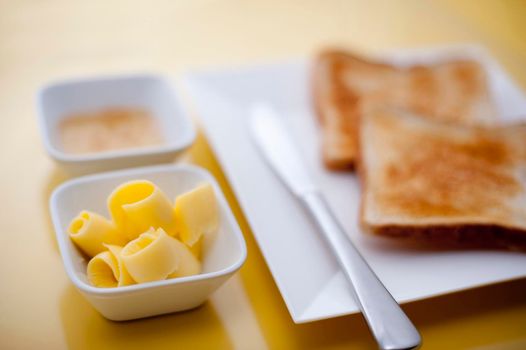 Toast with butter curls and marmalade laid out in individual containers on a wooden chopping board for a tasty breakfast
