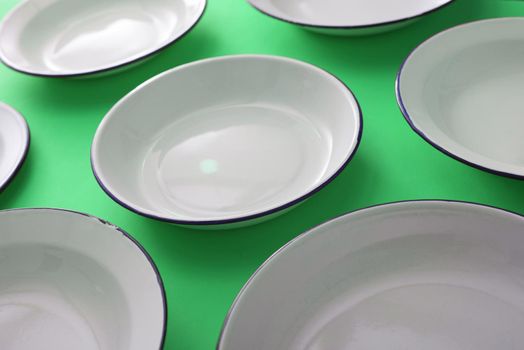 Clean white enamelled plates spread out on a colorful green background in a close up view