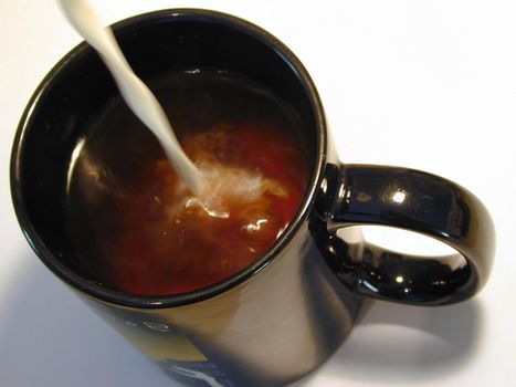 High angle view looking into the mug of a person pouring milk into a mug of black coffee