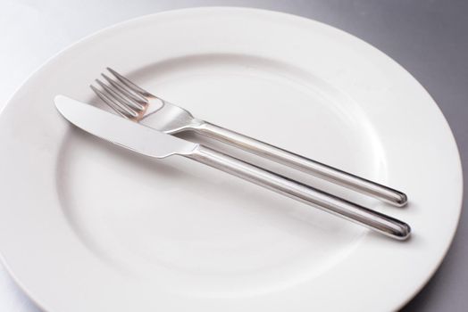 Plain generic silver metal knife and fork on a clean empty white dinner plate in a close up view