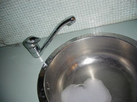 Tap and stainless steel sink with soap suds around the plug hole built into a countertop with tiled splash back
