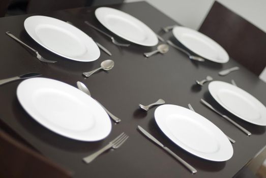 Place setting and generic white dinner plates with cutlery on a table with no food in a close up tilted angle view