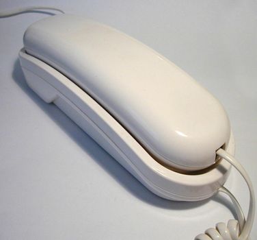 Single wired white round edged plastic telephone with shadow over gray background