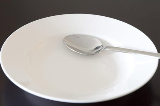 Empty clean white bowl and silver metal spoon in a close up view over black