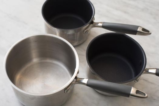 Clean empty cookware with assorted pots and saucepans in stainless steel and non-stick designs on a grey kitchen counter