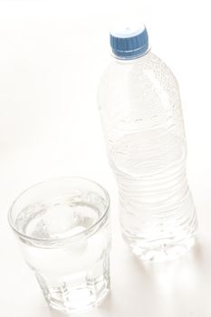 Bottled water served in a glass tumbler with the half full capped unlabeled plastic bottle alongside, high angle tilted view