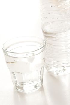 Glass of bottled water with a half full plastic bottle alongside on a white background with copyspace