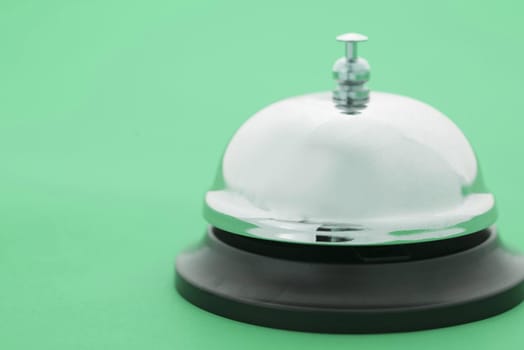Close up of a shiny, silver service bell isolated on a plain green background.