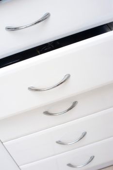 Row of white kitchen drawers with simple metal handles with one slightly open for storage of kitchenware