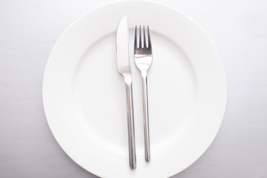 Empty generic white plate with silver knife and fork neatly placed in the centre viewed from overhead