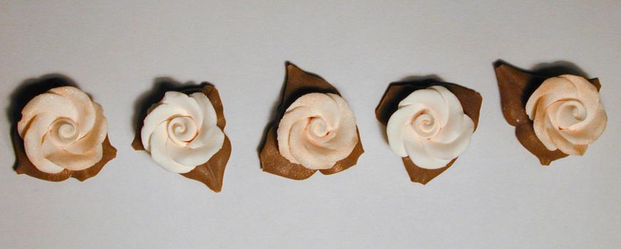 Row of white icing flowers used in baking to decorate a cake viewed from overhead on a grey background in banner format
