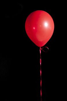 a single red balloon tied with ribbon floating in the air against a black backdrop