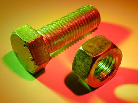 New metal bolt and nut in green and red lights on yellow surface, viewed in close-up from high angle