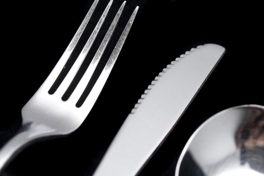 Clean silver metal knife and fork in a close up cropped view on a black table in a dining and food concept