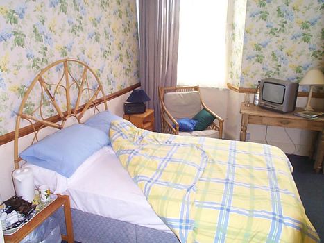 Neatly folded back bed in a blue bedroom with pretty floral wallpaper, a bamboo headboard and a retro television set