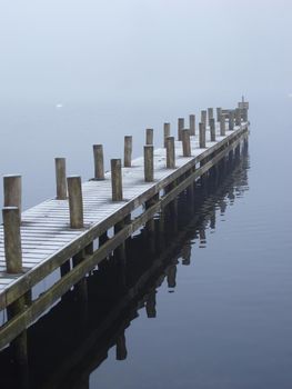 a jetty sticking out on to a still misty lake, calming and soporific