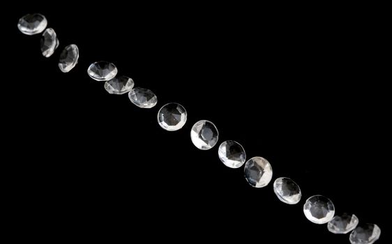 Diagonal line of faceted diamonds or gems sparkling against a black background with copy space on either side