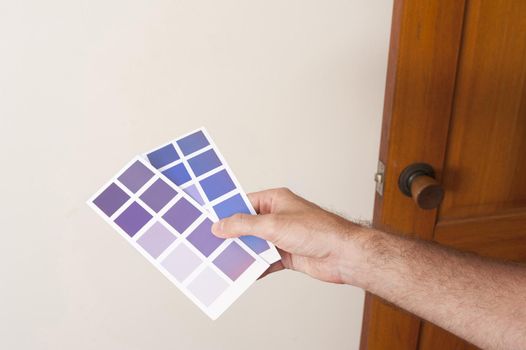 Man holding up blue paint swatches on cards against a white wall as he plans his new color scheme while interior decorating