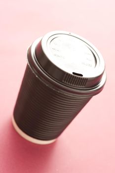 Disposable plastic mug of takeaway coffee or hot beverage with a closed lid viewed high angle on a pink background