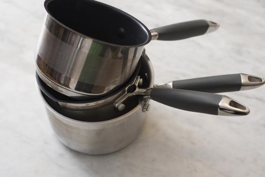 Stack of three metal non-stick kitchen pans or cookware with handles over a light grey background viewed high angle