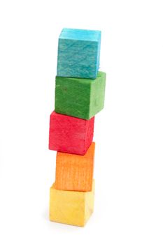 Wooden toy building blocks, in bright colours over white background, stacked in a tower