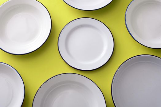 White metal enamel plates arranged on a colorful yellow background viewed from overhead in a full frame view